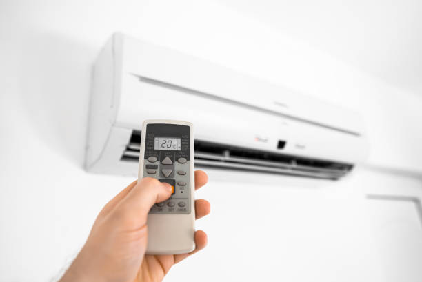 Hand holding remote control in front of the air conditioner.